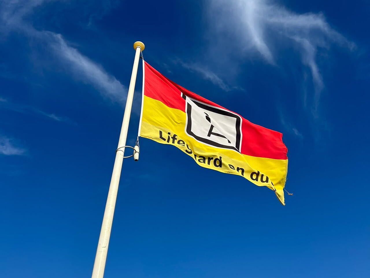 Een rood-gele vlag op het strand die aangeeft dat de lifeguards aanwezig zijn